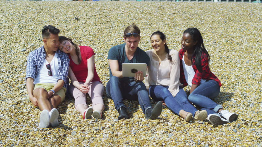 4k Happy mixed ethnicity group of friends using computer tablet at the beach