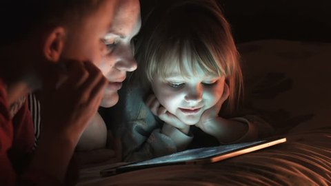 Blonde woman with her two kids lying on bed while watching cartoon on digital pad or tablet