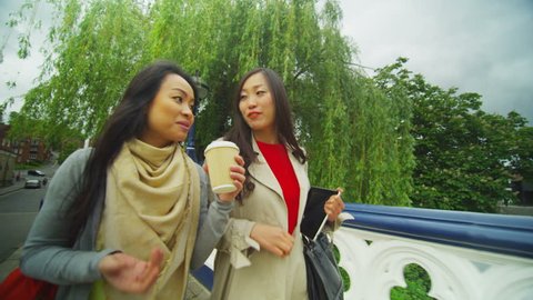 Attractive Asian female friends chatting as they walk together through city