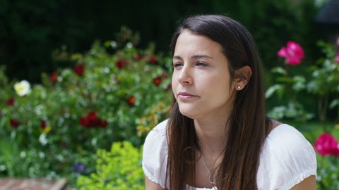 4K Woman with hay fever sneezes into a tissue as she sits in her garden