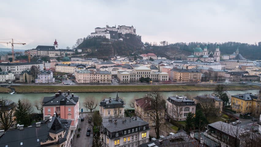 View of Salzburg, Austria at night. Illuminated Castle at the background, reflection in the river. Dark fast pacing sky, time-lapse