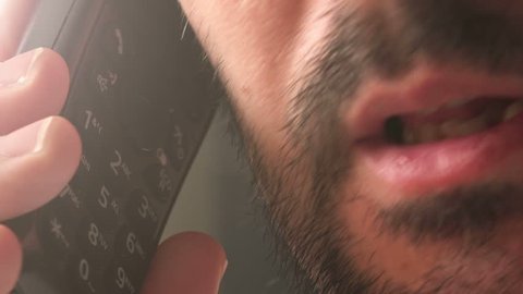 Unshaven adult caucasian male having private conversation over landline telephone, close up detail of face, beard and mouth talking.