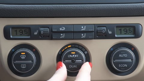 Closeup of young woman turning car air conditioner switch