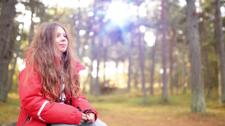 Beautiful smiling little girl with long hair in a red jacket on background of the autumn city park.