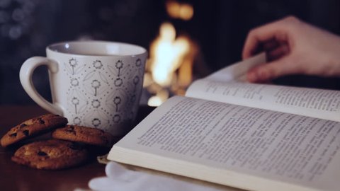female hands putting a book near a cup of tea by the fireplace