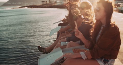 Group of hipster friends eating pizza sitting on the dock at the harbor during a summertime road trip