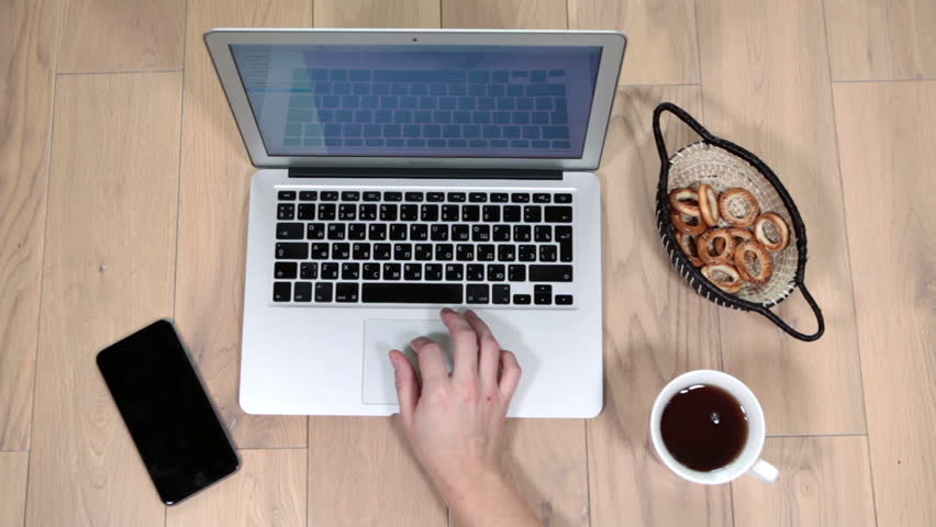 Female Caucasian hands using contemporary laptop, eating snacks and drinking coffee, view above