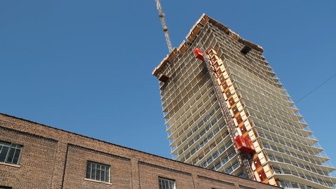 Condo construction. Timelapse. Timelapse of condominium being built in Toronto, Ontario, Canada. Elevator goes up and crane lowers bucket. Old brick building in the foreground.