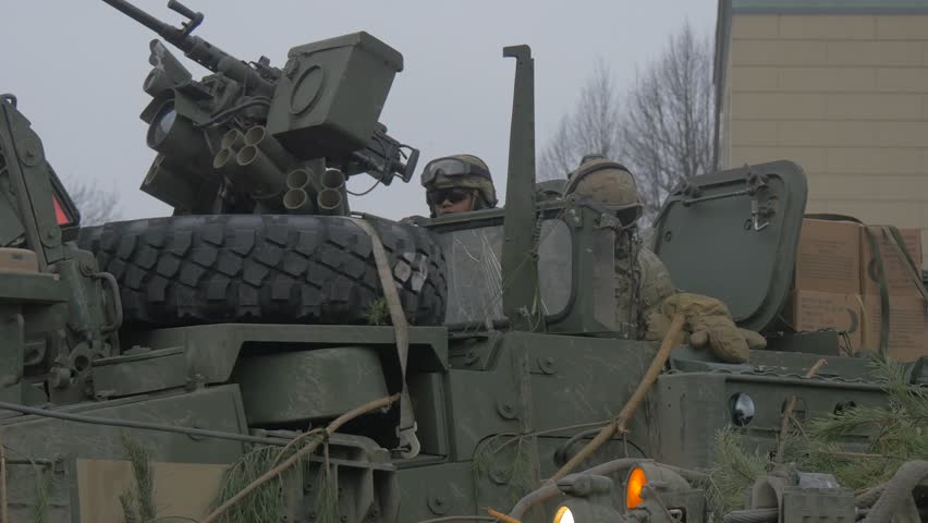 Two Soldiers in Camouflage Are Sitting in a Tank, Looking Around, Men in Militari Uniform on a Tank, Men in Helmets and Protective Glasses, Open Hatch, Weaponb Launcher on a Tire is Fixed on Panzer