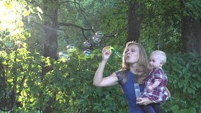 Nanny woman blow soap bubbles and baby girl look at them in beautiful sunset light in park. Static shot. - Powered by Shutterstock - Get 15% off with code: PIKWIZARD15