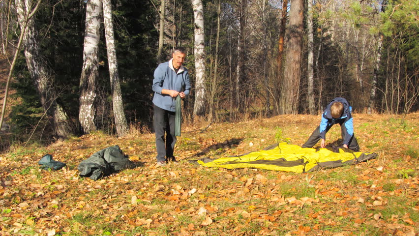 father and son installing tent in autumn forest