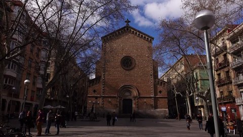 BARCELONA, SPAIN - FEBRUARY 28, 2016: Move closer to old Gothic church, dolly shot across small Barcelona square, Vila de Gracia neighbourhood. Cool february time, naked trees, sunny day, glide camera