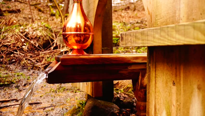 Man filling a bronze jug with clear forest water. Picturesque slider shot.
