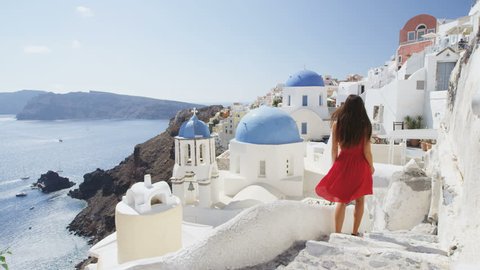 Elegant woman walking down stairs in Oia Santorini. Female tourist is in red dress on sunny day. She is visiting the famous tourist attraction destination on Europe travel. RED EPIC SLOW MOTION.
