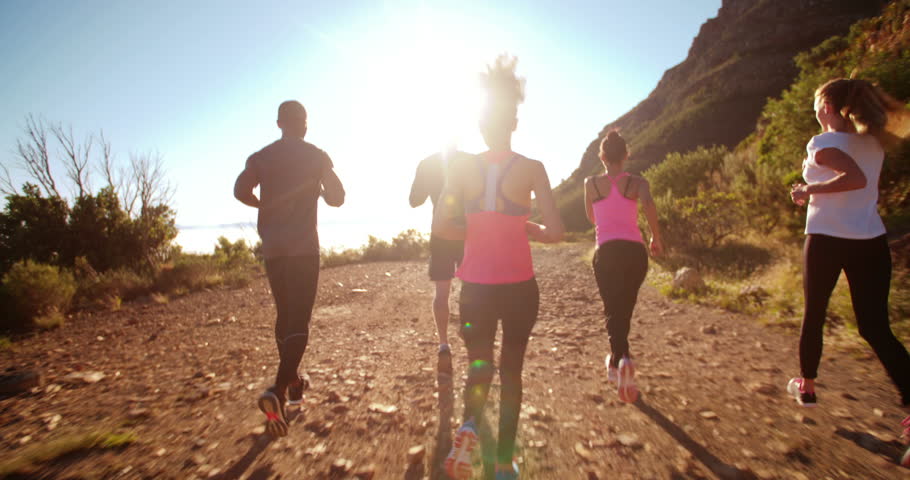 Back view of a group of friends jogging outdoors on a summer afternoon with sun flare