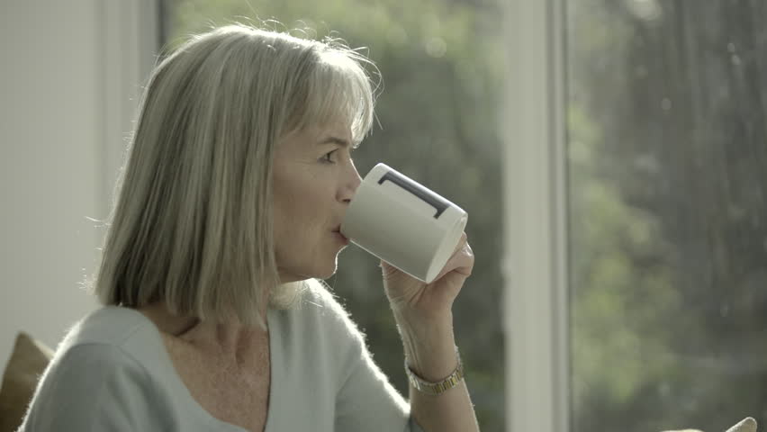 Beautyful retired senior woman with cup of tea looking at of window