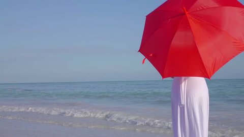 Elegant woman in white dress walking beach with red umbrella. Beautiful woman having fun on the beach in the Florida Keys. 