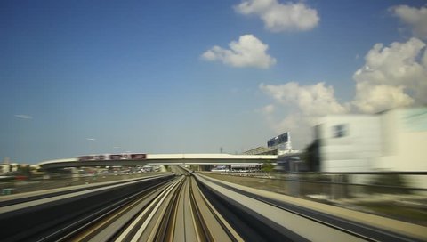 FPV ride at elevated railway, driver cabin view, oncome train sweep past. Dubai Metro rush along overground rails, low rise building around, motion blur, smooth time lapse. Nice blue sky, white clouds