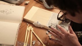 A series of clips of young woman prepares wooden plank with gypsum to paint on it. Girl works with a flat sculpture on a wooden board
