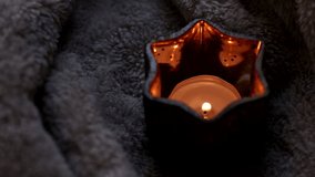 burning candle on fluffy blanket background