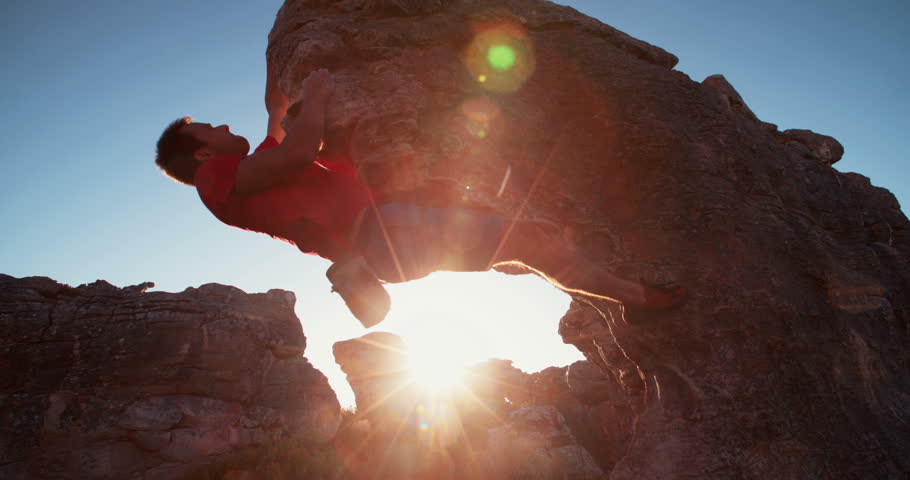 Bouldering climber man puts hand into bag full of chalk for grip while climbing rock wall on mountain at sunset or sunrise.