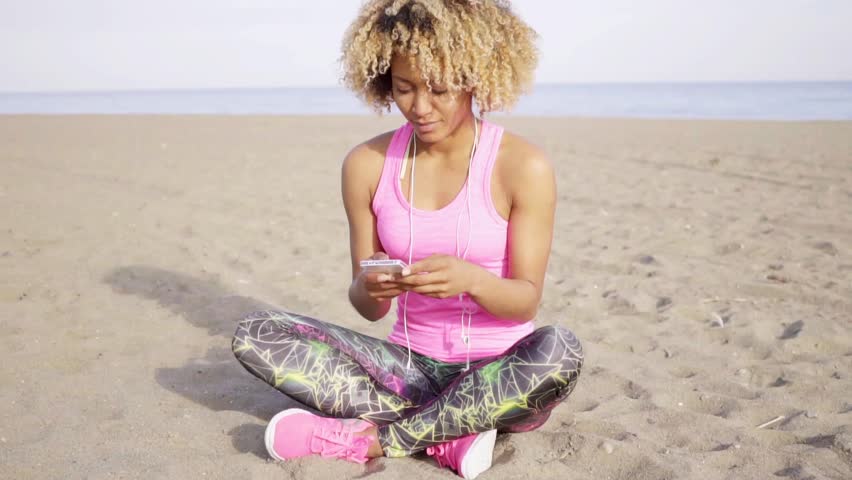 Grinning woman sitting on beach listening to music
