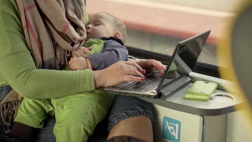 Mother holding sleeping baby and using PC in the train 
