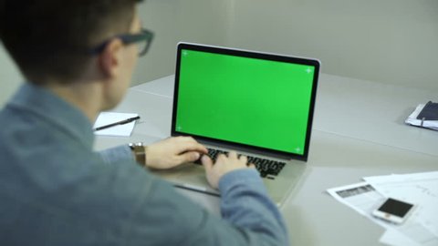 young man working on his laptop in a office. Green screen 