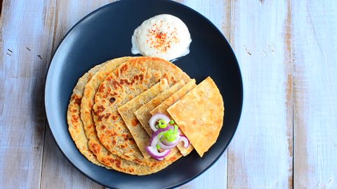 Indian/ Pakistani woman hand serve a platter of Paratha flatbread with red and spring onion and yogurt. Food background and texture