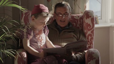 A grandfather is reading a story book to his grandson. The grandson is dressed up as a princess from the story in the gender blender style. Shot in a modern British house.