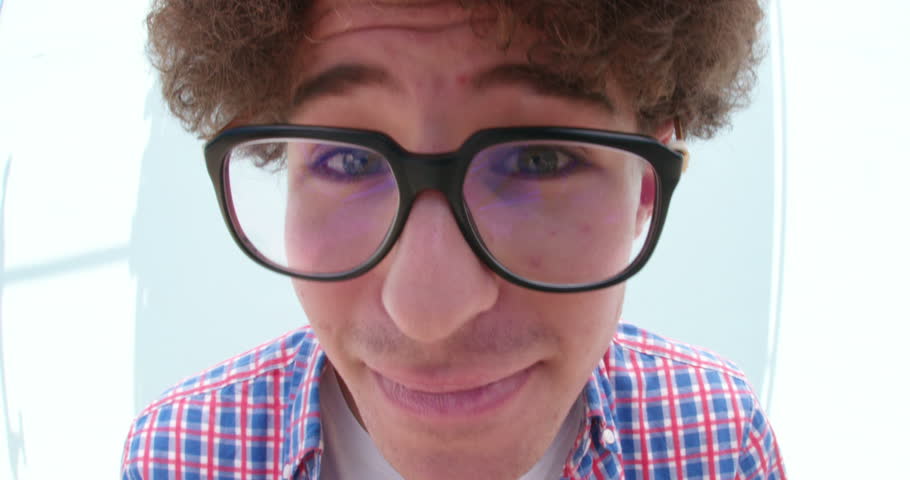 Teenager boy posing and making silly faces, isolated on blue wall background with fisheye lense effect