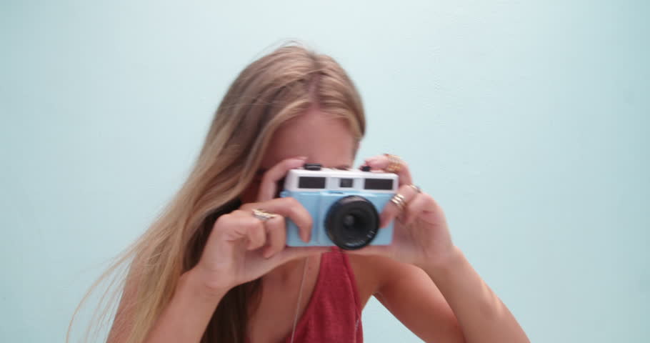 Beautiful woman with long blue hair holding a retro blue camera, isolated on blue wall background