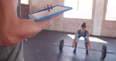 Small group of multi-ethnic athletes engaged on dead lifting during a crossfit workout at the gym. They got tought by their personal trainer with digital tablet