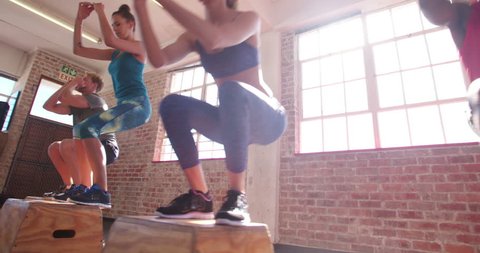 Multi-ethnic group of friends jumping onto wooden boxes in a crossfit training