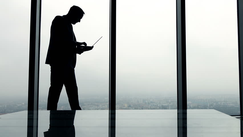 Silhouette of businessman working on laptop standing by window in the office, 4K
