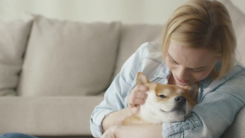 Happy blond woman is playing with pet dog at home next to a sofa. Shot on RED Cinema Camera in 4K (UHD).