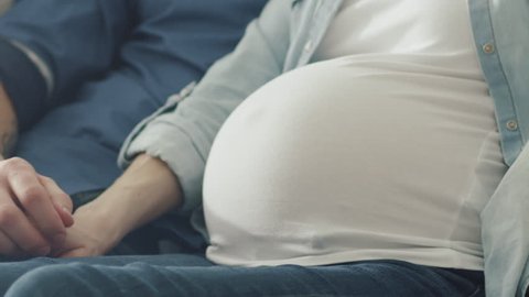 Pregnant blond female and a man relax on a couch at home. Shot on RED Cinema Camera in 4K (UHD).