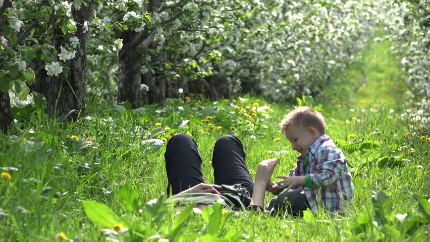 Mother hands tickle blonde little boy in flourish orchard, laughing and having fun