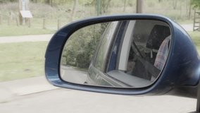 A slow motion shot of a wing mirror of a moving car with the reflection of a baby girls face whilst sat in the baby car seat.