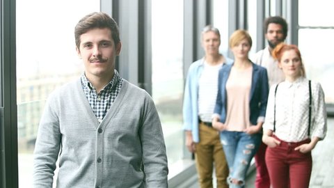 Portrait of young male advertising executive smiling, colleagues in background, slow motion, graded
