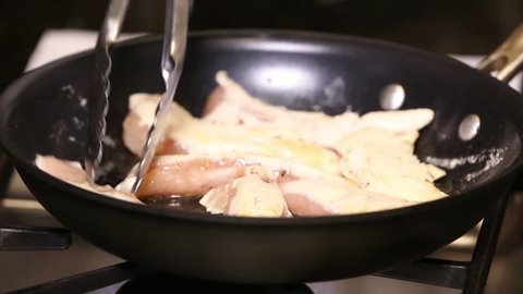 A woman turns over chicken and adds seasoning, close up