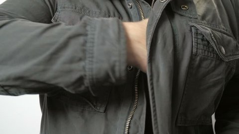 Slow motion shot of a man in a jacket reaching into it and pulling a handgun out.