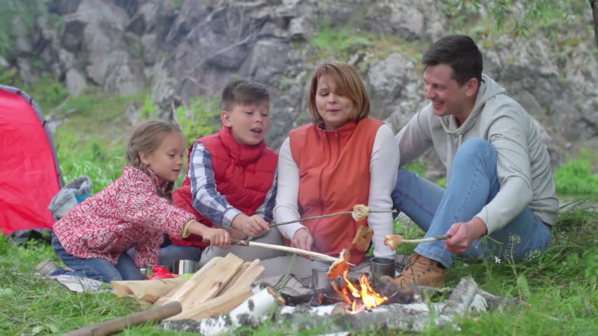 Mother, father, son and little daughter making bread over campfire and talking