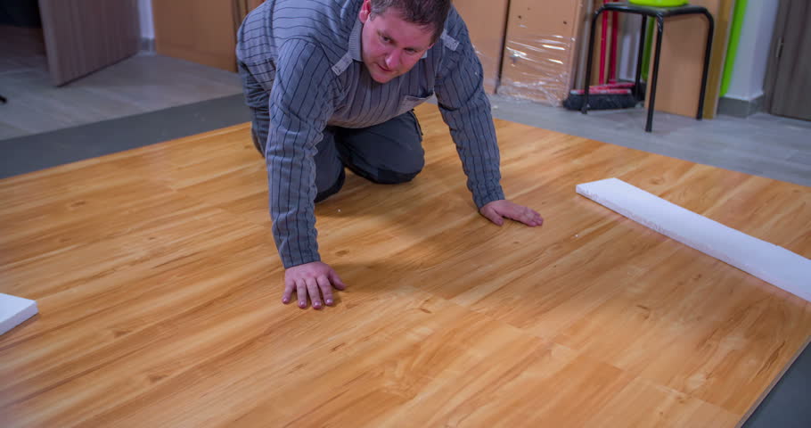 A man is making sure there are no bumps in the new flooring. He is satisfied with his work and he shows thumbs up.
