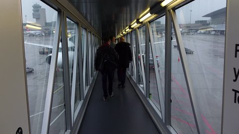 ZURICH - FEBRUARY 29, 2016: POV walk through jet bridge, boarding to airliner, look out to apron area, rainy weather outside. Unidentified passengers come ahead, Zurich Airport, morning time flight