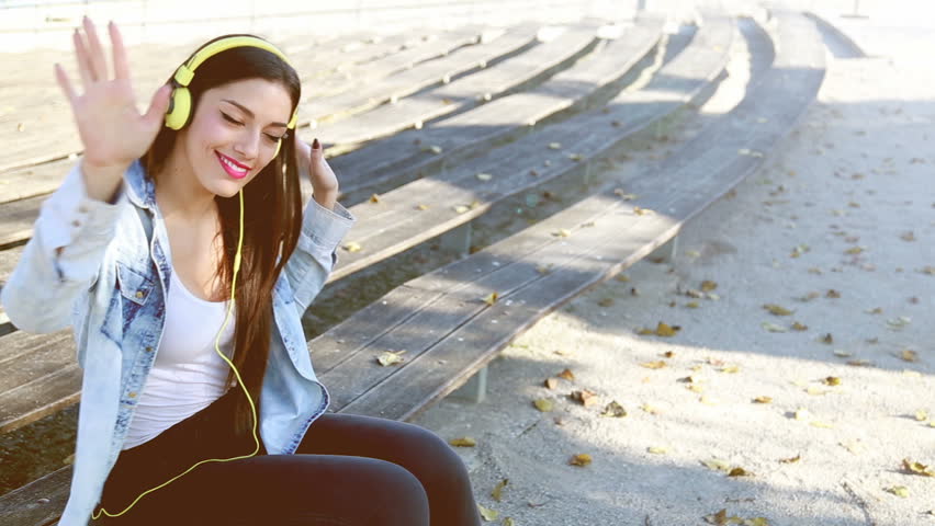 Beautiful brunette woman listening to music on headphones and dancing to the rhythm at park, graded