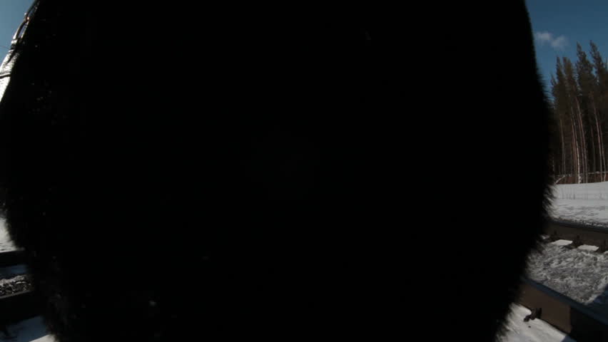 Adult woman wearing fur coat stepping away from camera on winter railroad in forest