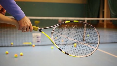 Hands of coacher training to girl to hold racket. Net and children out of focus