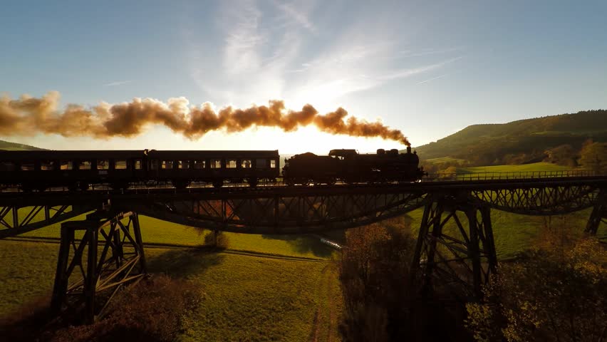 Nostalgic steam engine locomotive crossing bridge at sunset. old historical train technology background