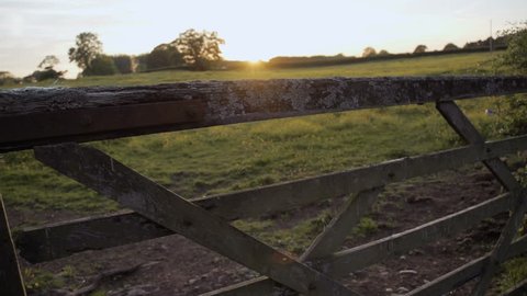 A sliding shot of the camera moving through an old wooden gate leading to a meadow at sunset.